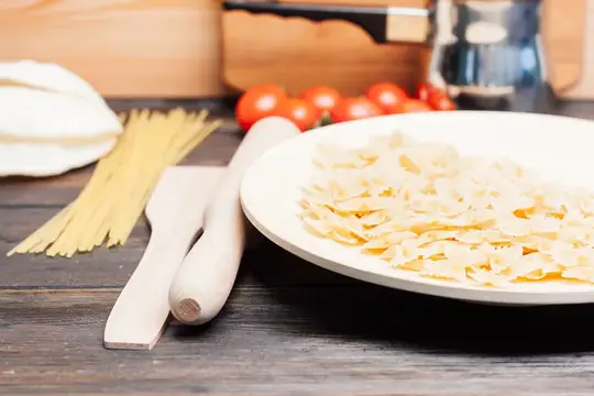 Свежая паста, деревянные лопатки и помидоры на кухонном столе