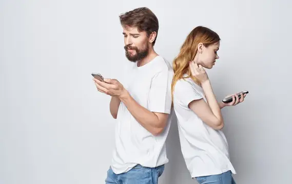 Мужчина и рыжеволосая женщина стоят спиной к спине со смартфонами