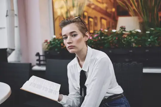 Молодая женщина с книгой сидит в летнем кафе