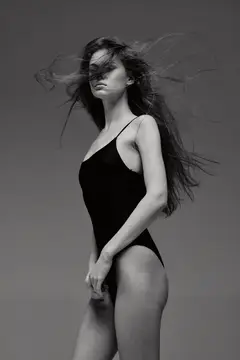 Стройная темноволосая женщина в чёрном купальнике на ветру