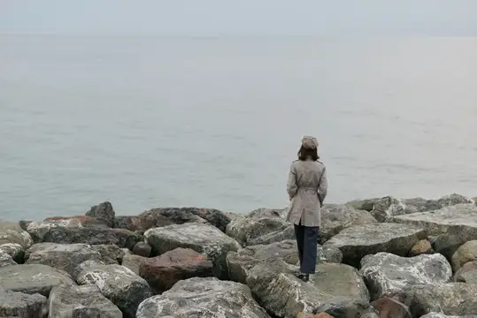 Женщина в плаще стоит на камнях у туманного моря