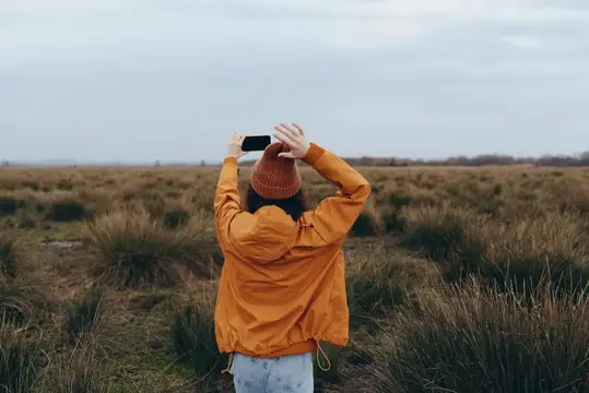 Девушка в оранжевой куртке фотографирует поле на телефон