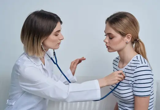 Женщина-врач слушает пациентку стетоскопом на приёме