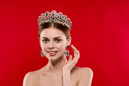 Молодая женщина в роскошной короне и серьгах на красном фоне