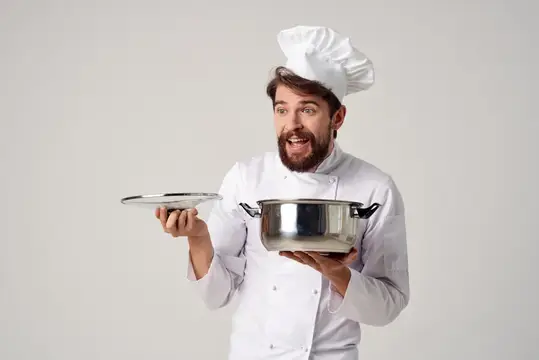 Удивлённый бородатый повар с кастрюлей и крышкой на сером фоне