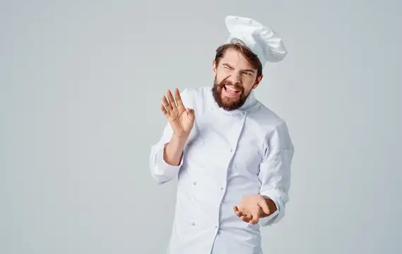 Профессиональный повар в униформе и головном уборе жестикулирует руками
