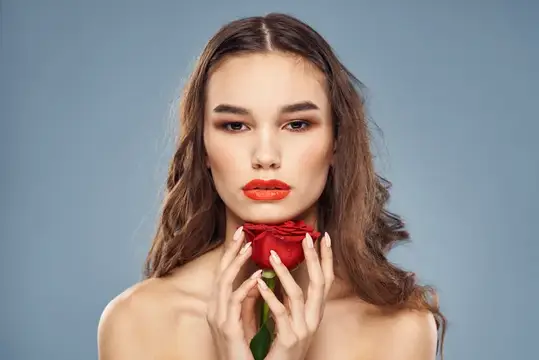 Молодая женщина с красной розой у лица на сером фоне