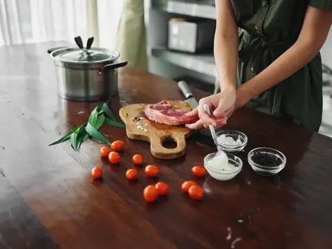 На кухне женщина готовит ужин из мяса, овощей и специй на деревянном столе на фоне стильной кухни, крупный план рук, образ жизни