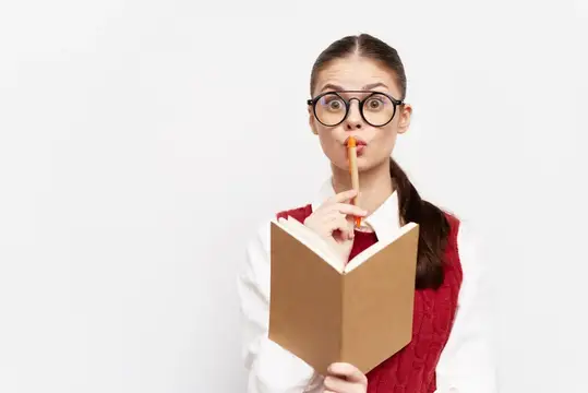 Студентка в красном жилете и очках держит книгу и карандаш у губ, подавая знак молчания