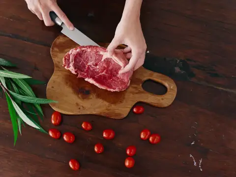 Руки нарезают кусок сырого мяса на деревянной доске