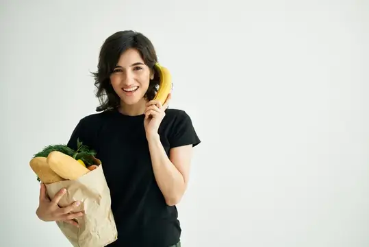 Улыбающаяся брюнетка с пакетом продуктов говорит по банану