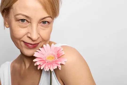 Улыбающаяся женщина с розовой герберой у плеча