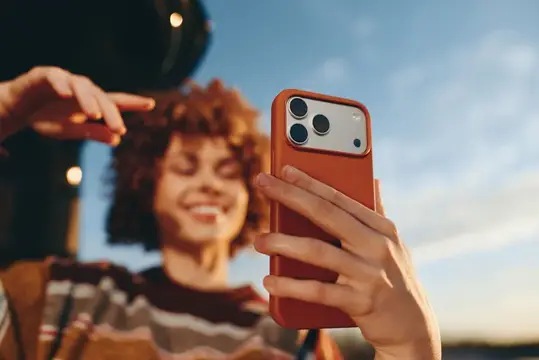 Кудрявая девушка делает селфи на смартфон в оранжевом чехле