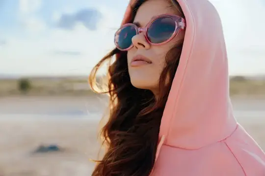 Молодая женщина в розовом капюшоне и солнцезащитных очках на пляже