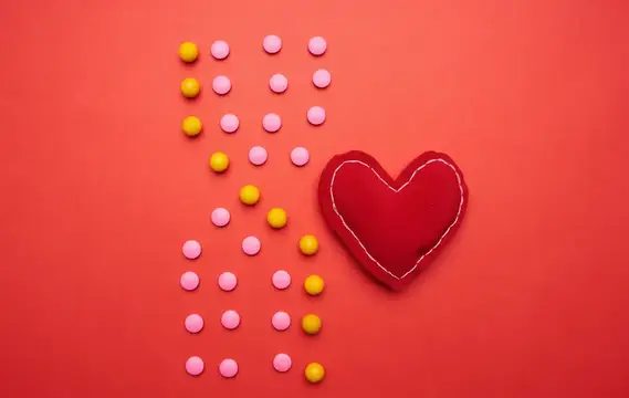 Красное сердце и цветные конфеты на красном фоне