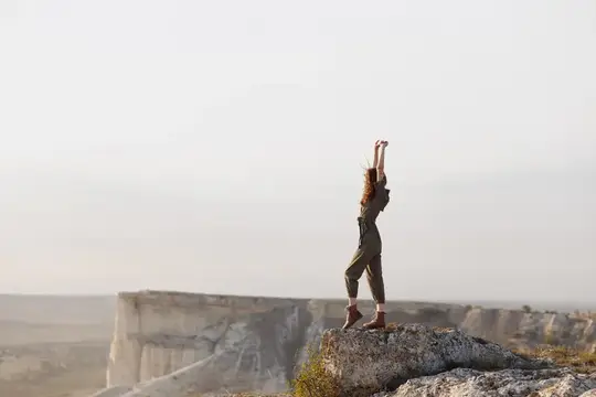 Женщина стоит на вершине горы с поднятыми руками