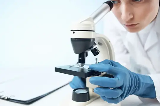 Женщина-врач в медицинской маске работает с микроскопом, используя современные технологии для исследований