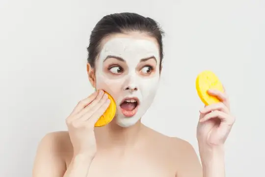 Удивлённая девушка с белой маской на лице и жёлтыми спонжами