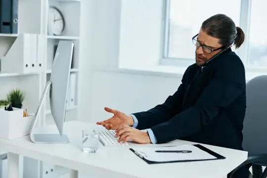 Мужчина в очках с длинными волосами работает за компьютером в офисе