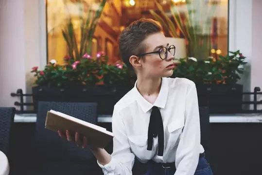 Девушка с короткой стрижкой и книгой у кафе