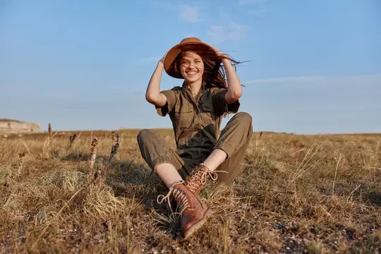 Улыбающаяся девушка в шляпе сидит в сухом поле