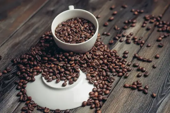 Белая чашка с кофейными зёрнами на тёмном деревянном столе