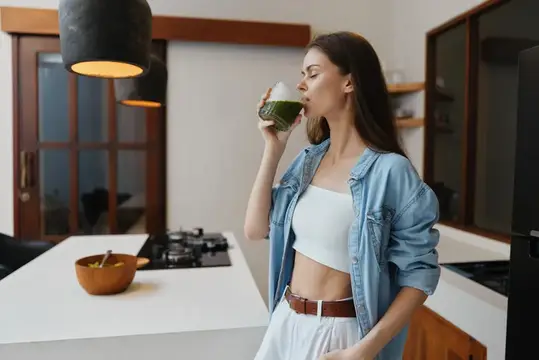 Молодая женщина пьёт зелёный смузи на светлой кухне