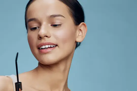 Улыбающаяся девушка с тушью для ресниц на голубом фоне