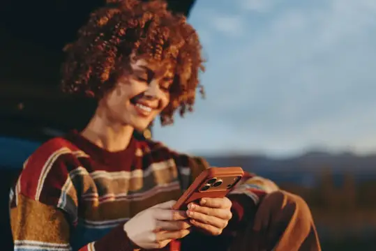 Улыбающаяся кудрявая девушка со смартфоном на закате