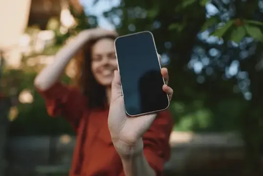 Улыбающаяся женщина показывает смартфон на фоне зелени