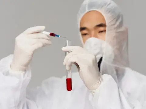 Лаборант в защитном костюме набирает красную жидкость в пробирку