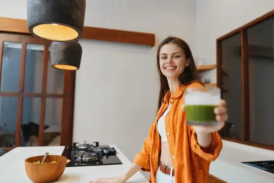 Улыбающаяся девушка с зелёным смузи на светлой кухне