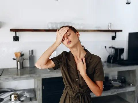 Уставшая женщина держится за голову на кухне