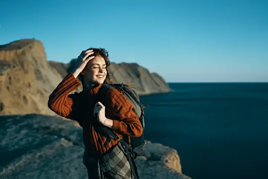 Улыбающаяся девушка с рюкзаком на скалистом берегу моря