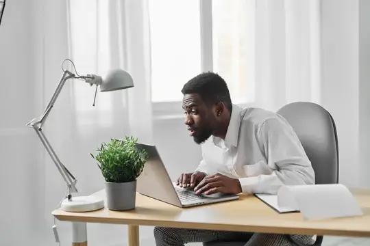 Удивлённый темнокожий мужчина работает за ноутбуком в светлом офисе