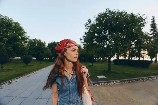 Молодая женщина в красной бандане гуляет по парковой аллее