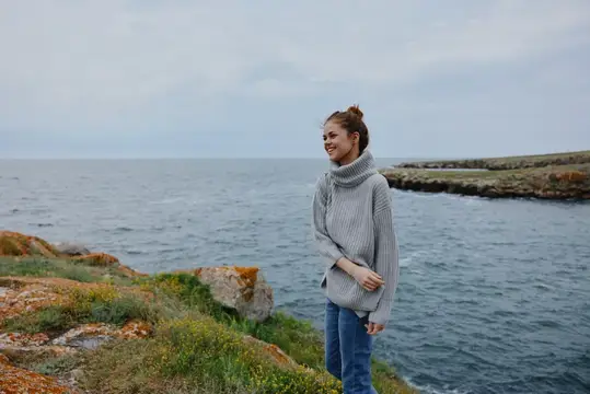Портрет женщины в свитере на фоне облачного моря, любующейся природой