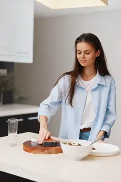 Женщина-шеф-повар готовит блюдо, нарезая мясо на деревянной разделочной доске на кухне