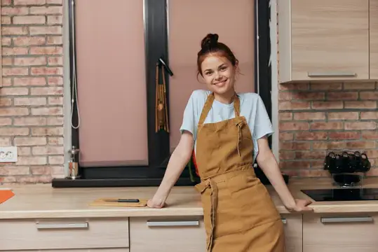 Молодая женщина в фартуке улыбается на кухне