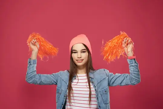 Улыбающаяся девушка в розовой шапке с помпонами на розовом фоне