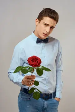 Красивый мужчина с красной розой, синяя рубашка, бабочка, светлый фон, обрезанный вид