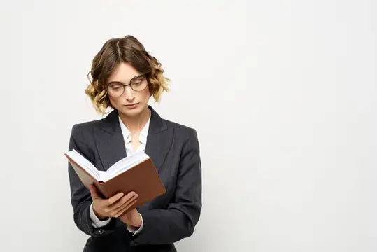 Девушка в очках и деловом костюме сосредоточенно читает книгу