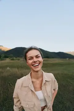 Смеющаяся темноволосая девушка на фоне гор и поля