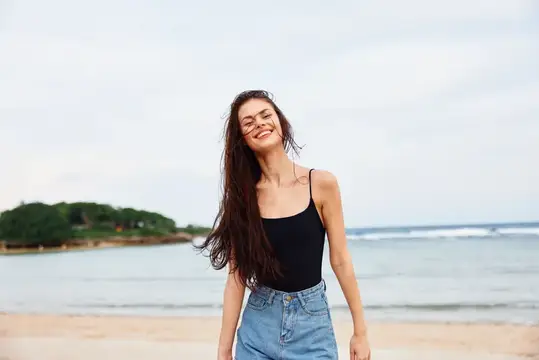 Улыбающаяся темноволосая девушка на песчаном пляже у моря