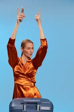 Молодая женщина в оранжевом платье с поднятыми руками и чемоданом