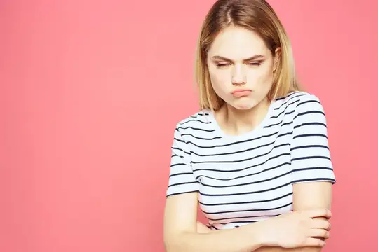 Недовольная блондинка в полосатой футболке на розовом фоне