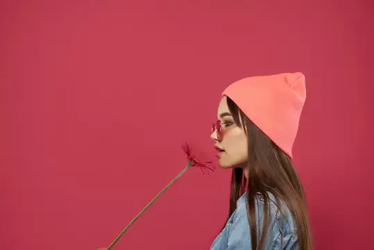 Молодая девушка в розовой шапке нюхает цветок на бордовом фоне