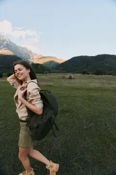 Улыбающаяся девушка с рюкзаком на горном лугу