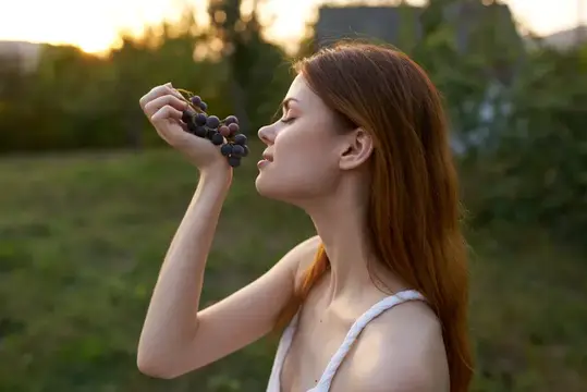 Женщина на природе, на открытом воздухе, ест виноград