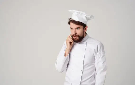 Задумчивый бородатый повар в белом колпаке на сером фоне
